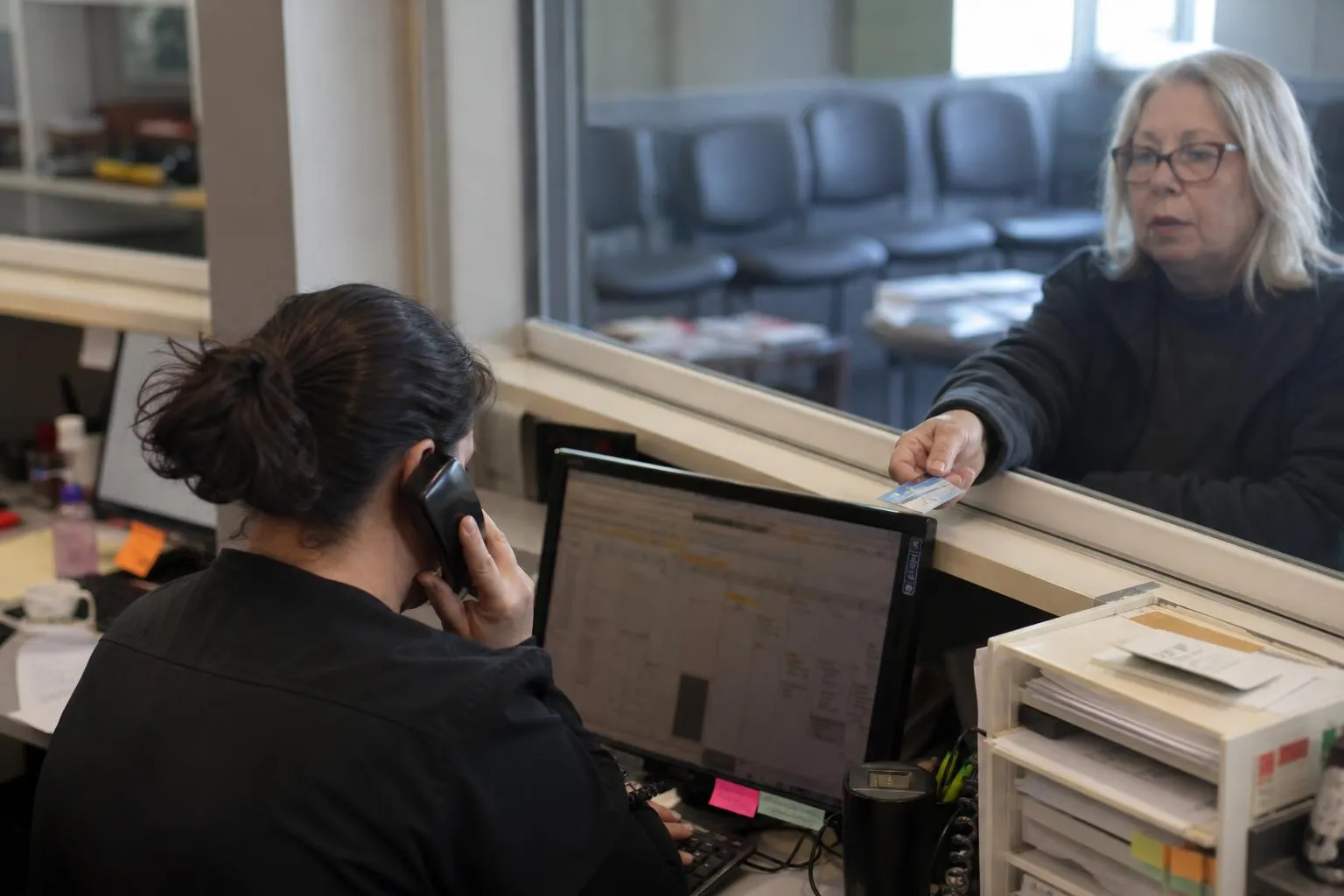 A dental front desk coordinator on a phone call while a patient checks in at the front window