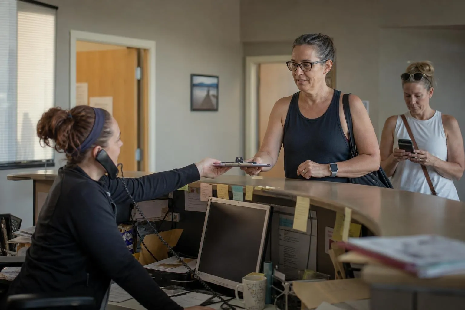 Front desk staff member at a busy chiropractic clinic reception desk with the phone ringing while checking in a patient