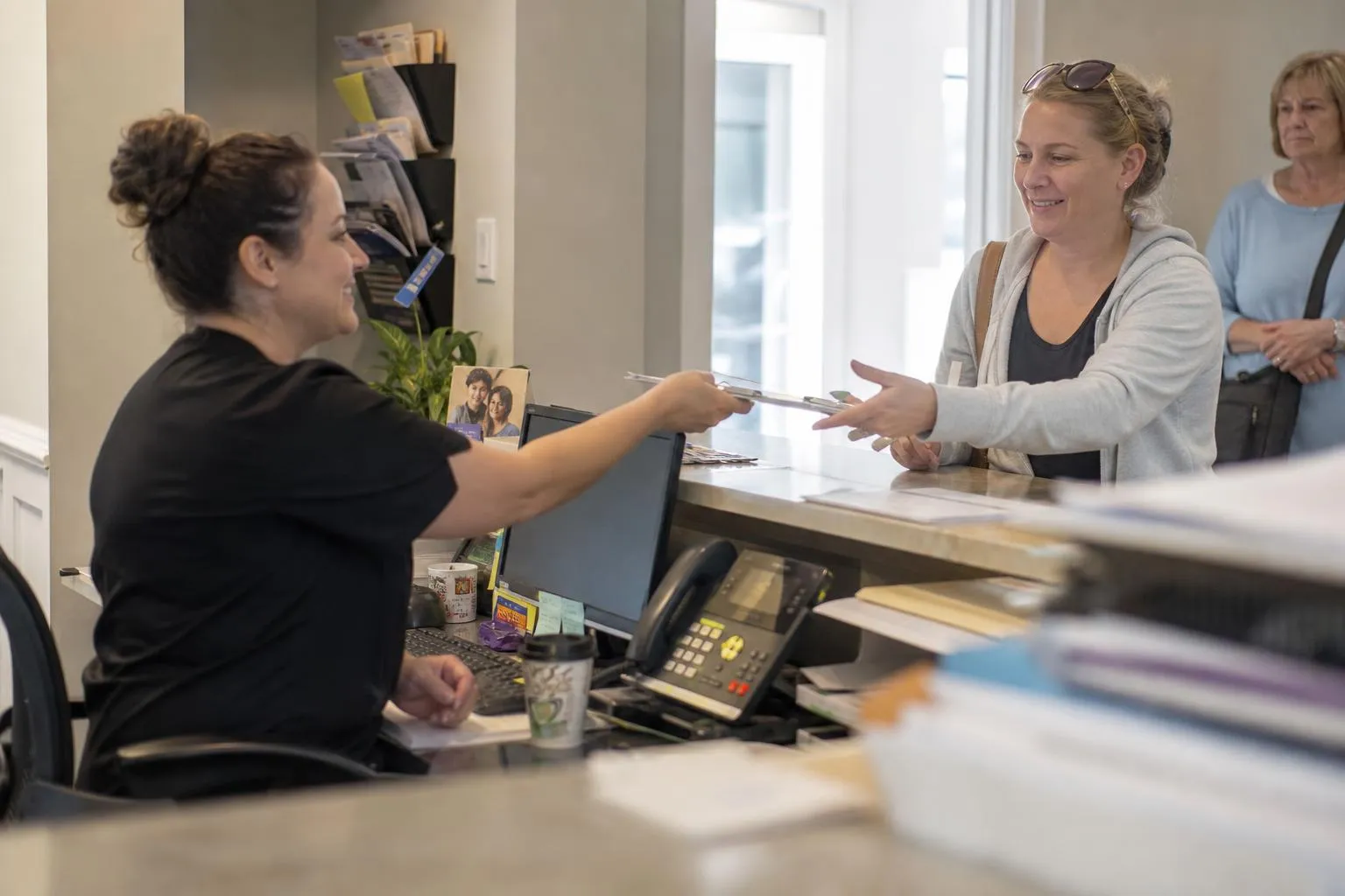 Dental front desk coordinator checking in a patient while the desk phone rings unanswered beside her