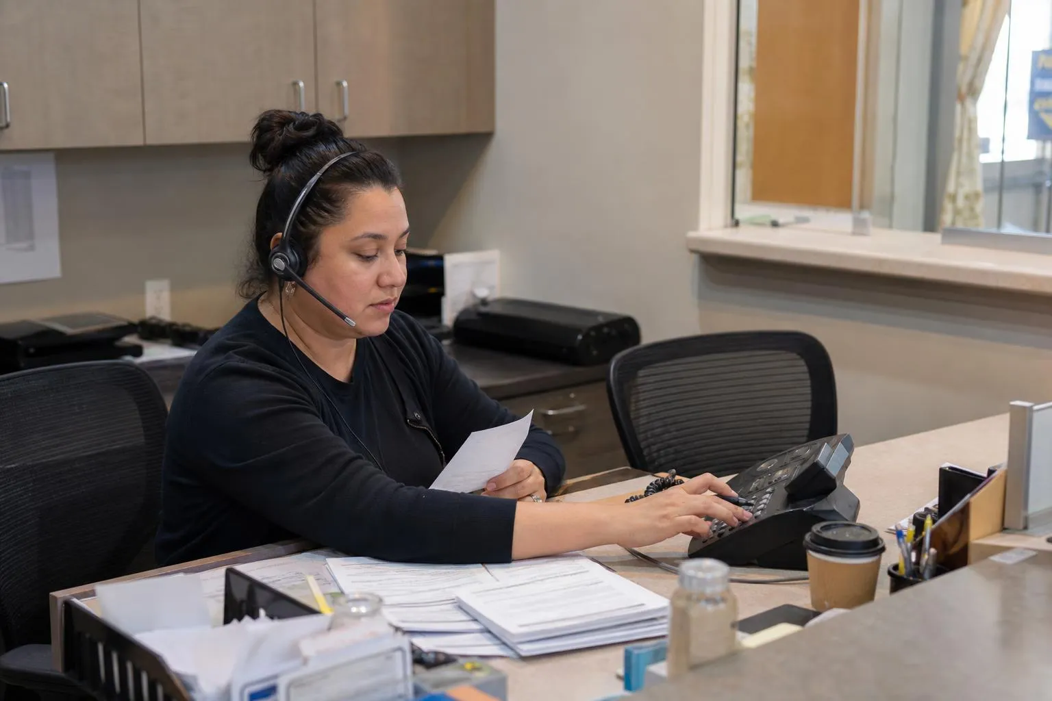 Front desk coordinator at a medical practice working through a stack of printed overnight messages beside a desk phone