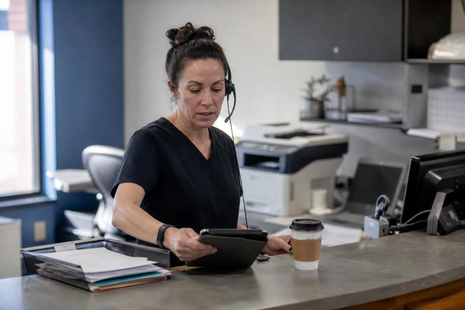 A clinic staff member at the front desk checks a tablet alert while a call is still in progress