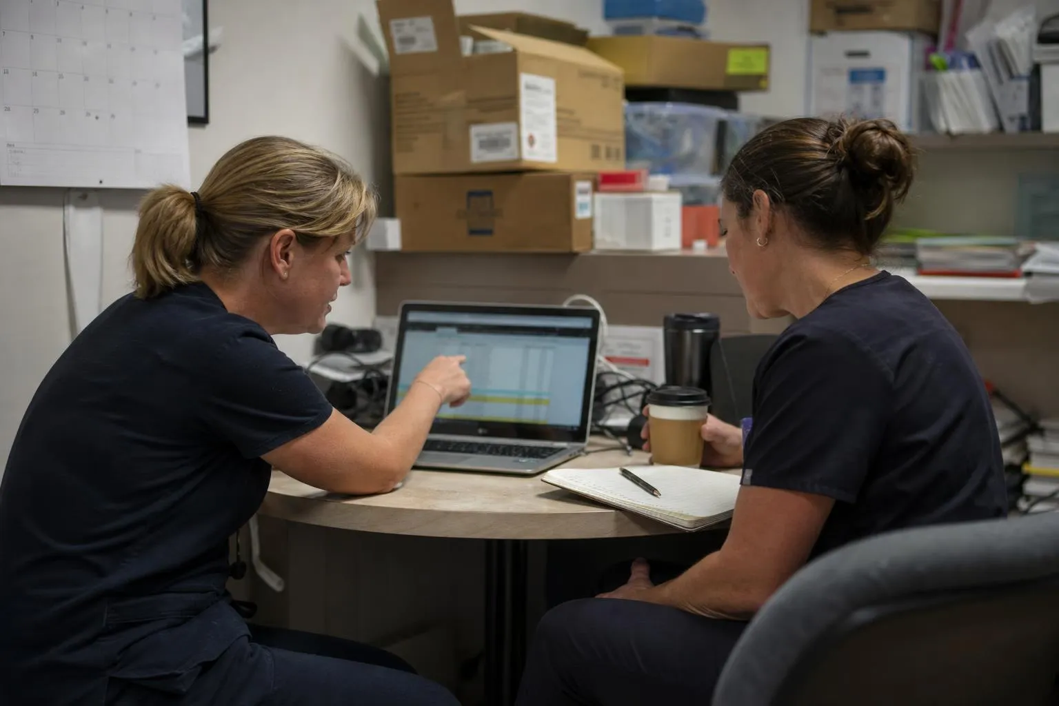 An operations leader and an office manager reviewing per-location recall results on a laptop in a dental practice back office