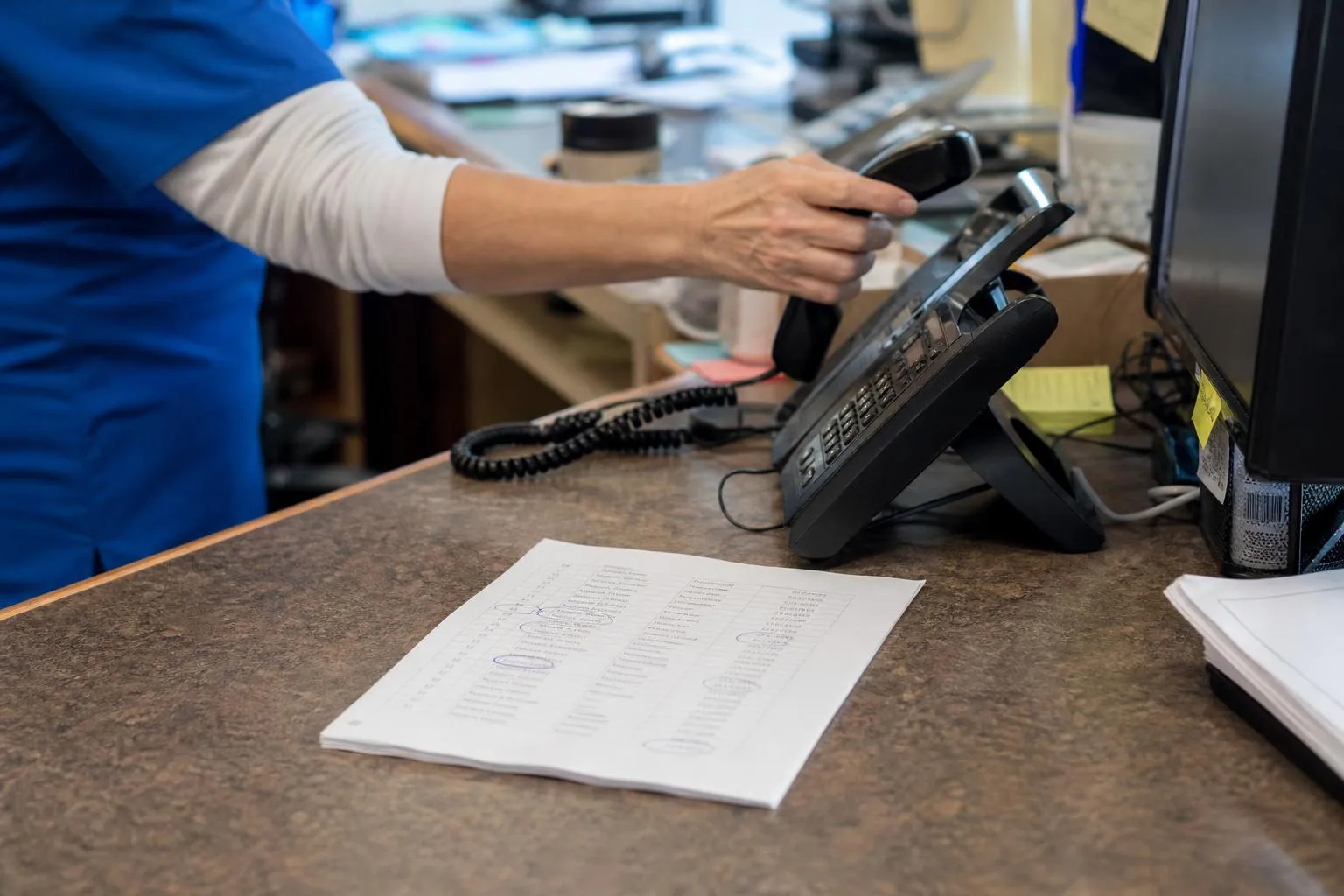 A printed recall list on a front desk counter next to a phone, with rows circled in pen