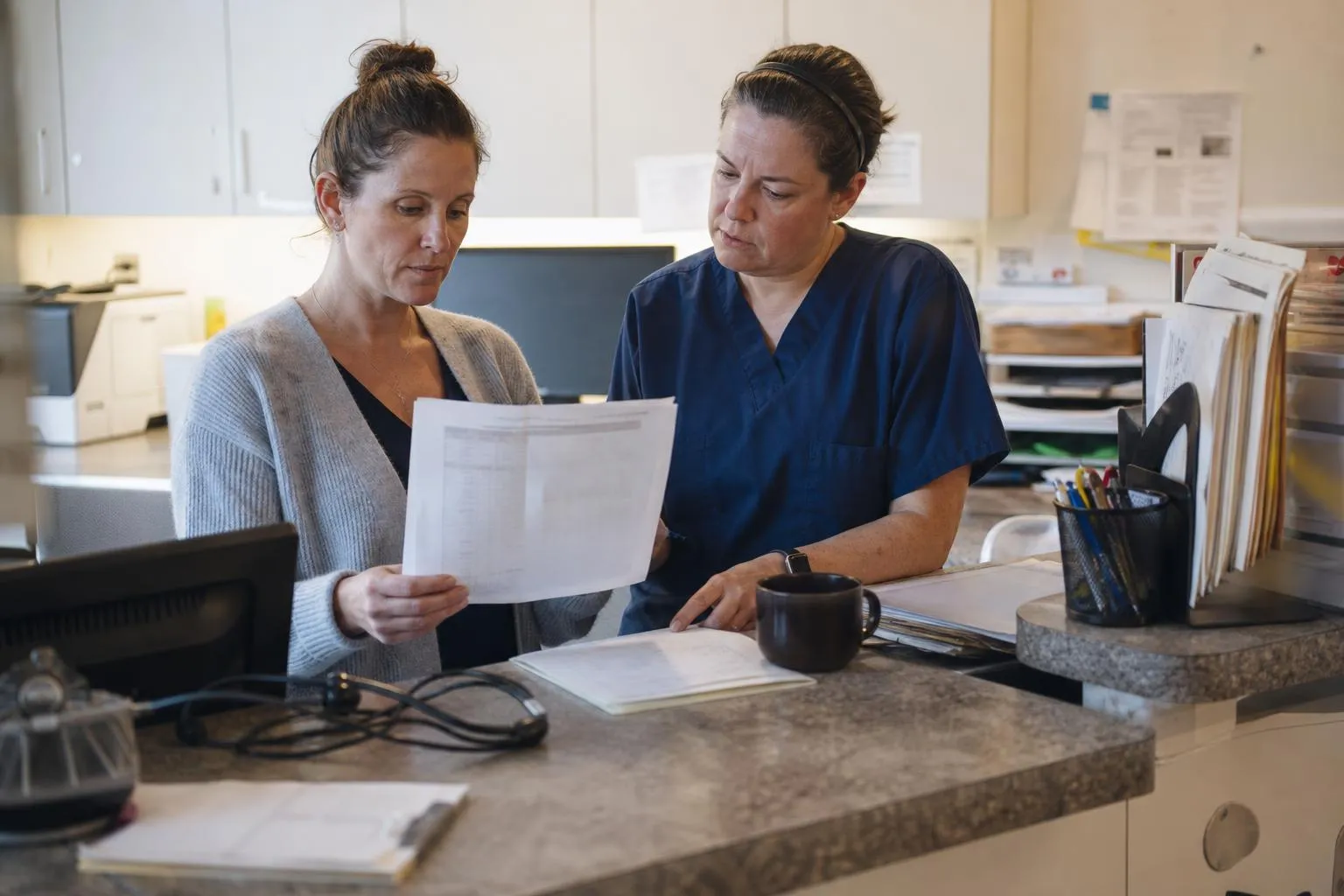 A clinic operations manager and site coordinator reviewing a weekly report at a reception counter