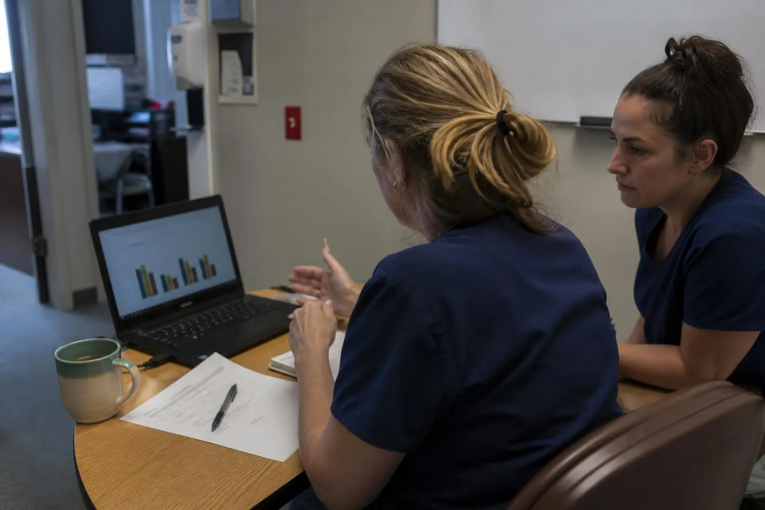 A practice administrator reviewing a monthly referral report on a laptop in a clinic back office