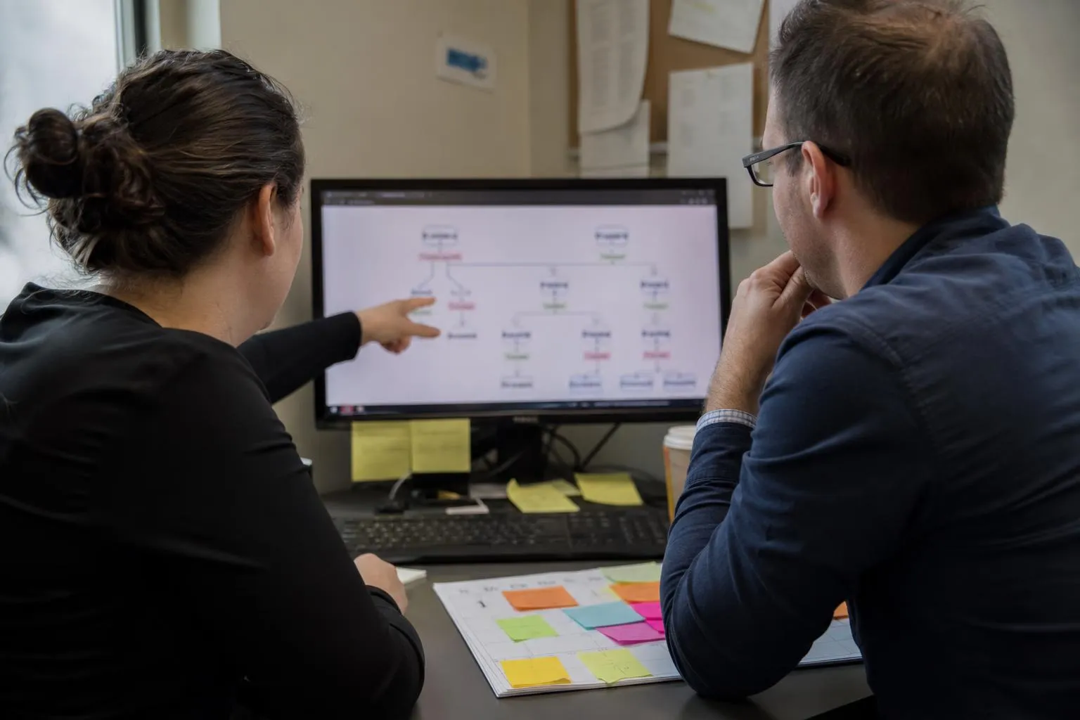A practice operations lead and an IT staff member reviewing a call workflow diagram on a monitor in a clinic back office