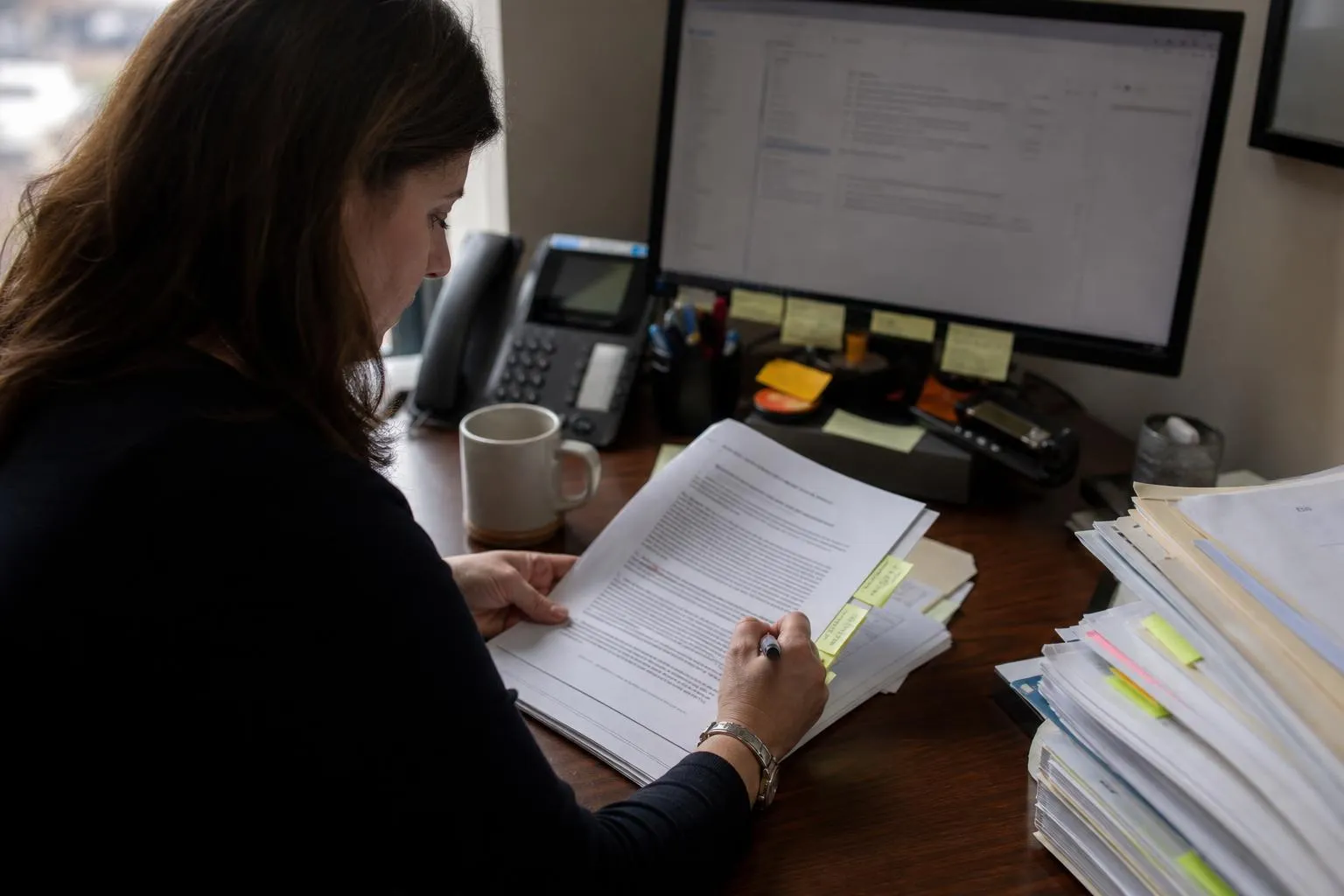A practice administrator reading a printed business associate agreement at her desk, pen in hand